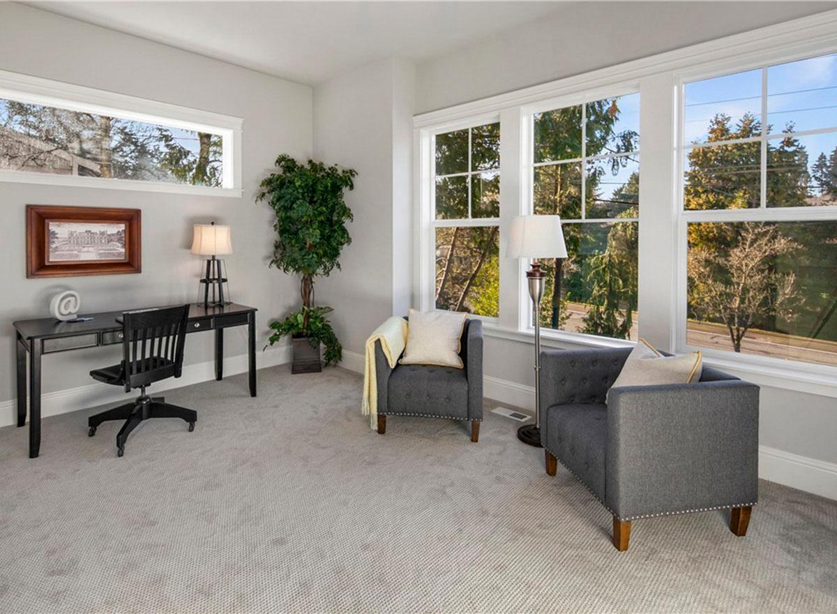 Interior rendering of a home office with a desk, chair, two armchairs, and large windows overlooking trees.