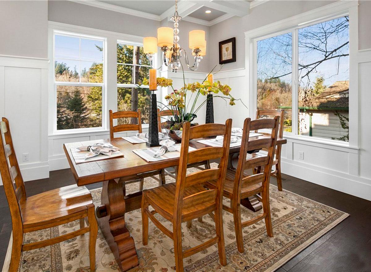 Dining room with wood table, chairs, chandelier, and large windows overlooking trees.