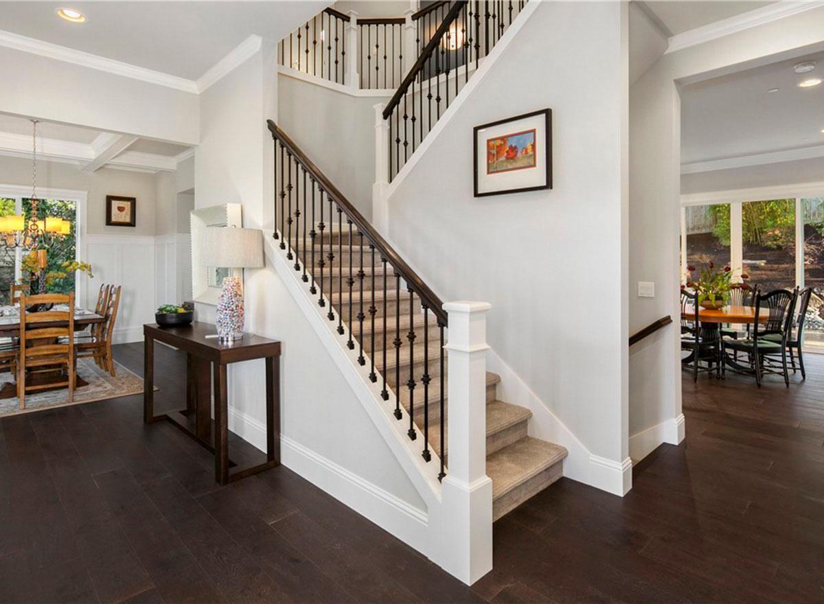 Interior view showing a staircase with dark wood banister and spindles, leading to upper levels. Dining area visible.
