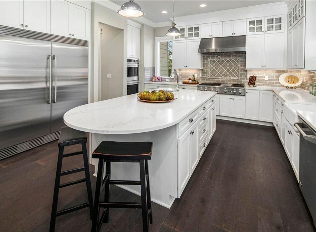 Modern kitchen with white shaker cabinets, large island, stainless steel appliances, gas range, and quartz countertops.