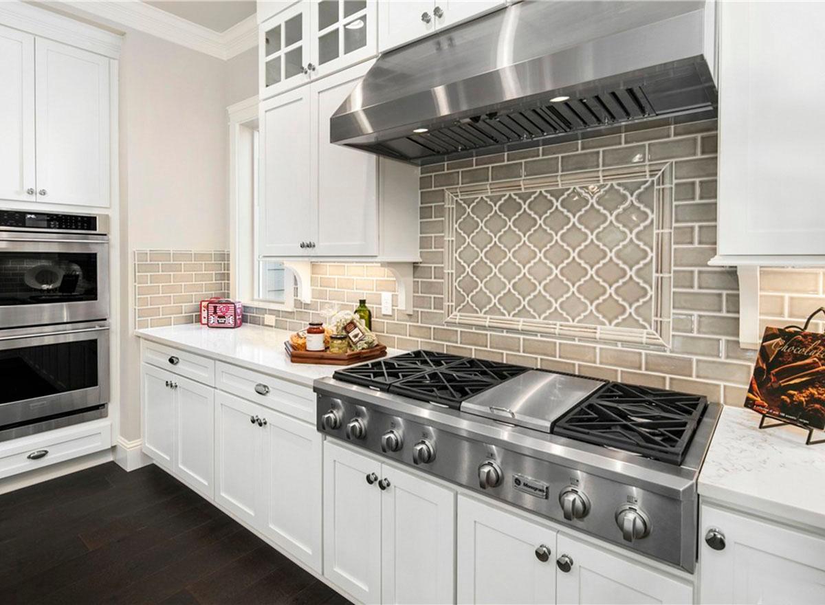 Kitchen with white cabinets, stainless steel appliances including double ovens and a range, and a tiled backsplash with a decorative insert.