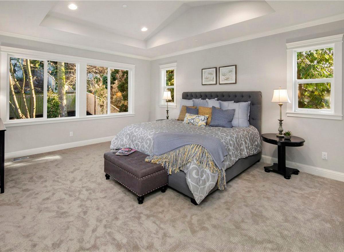 Bedroom with tray ceiling, multiple windows, tufted headboard, and upholstered bench.
