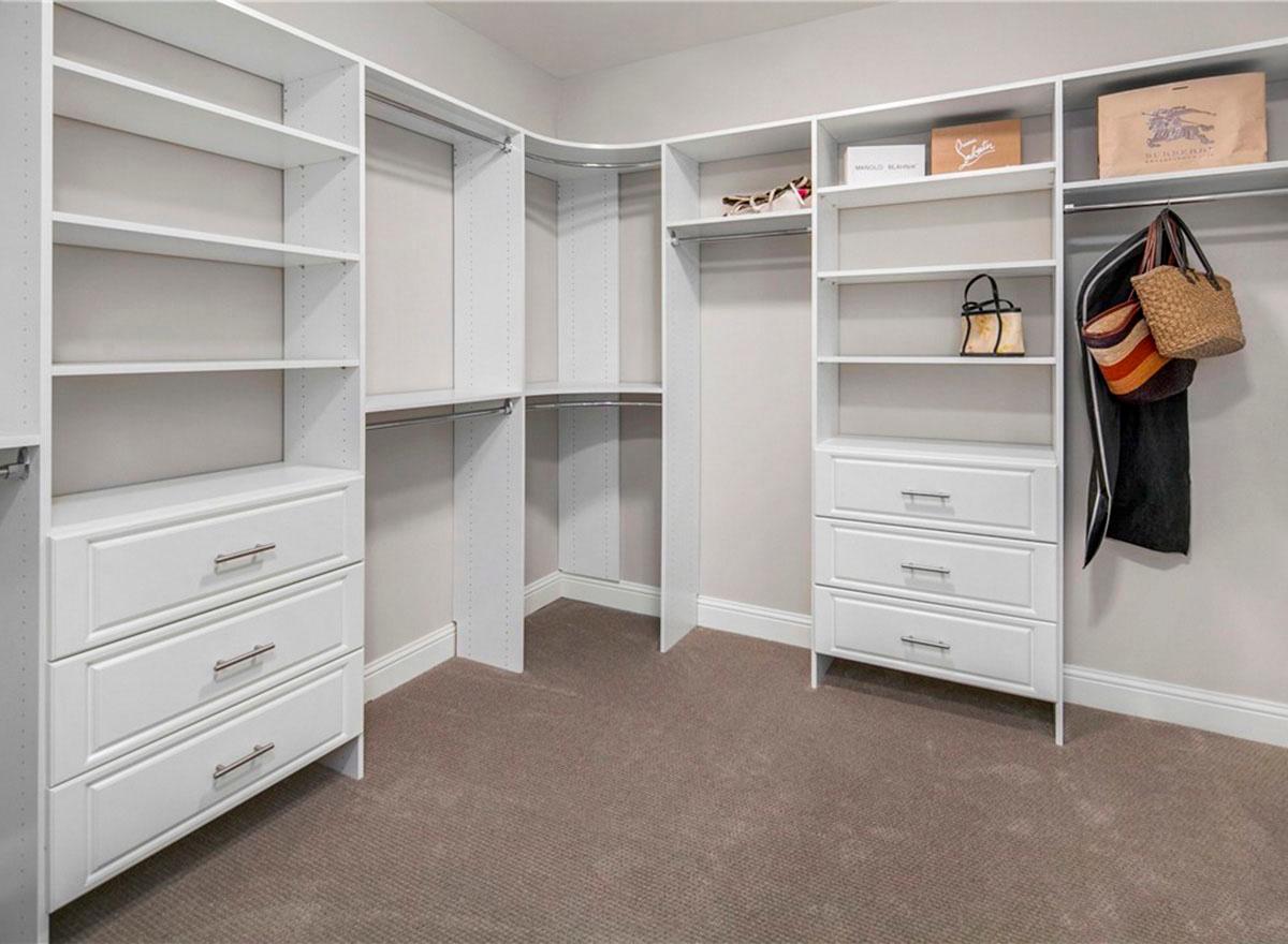 Walk-in closet with custom white shelving units, drawers, and hanging rods.
