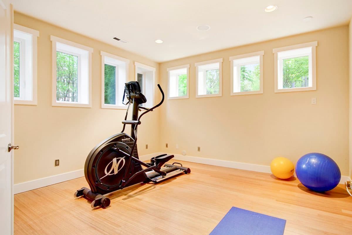 Interior view of a home gym with an elliptical machine, exercise balls, and multiple windows.