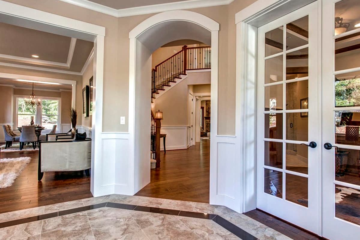 Interior view of house entryway with arched doorway to staircase, dining room, and glass-paned French doors.