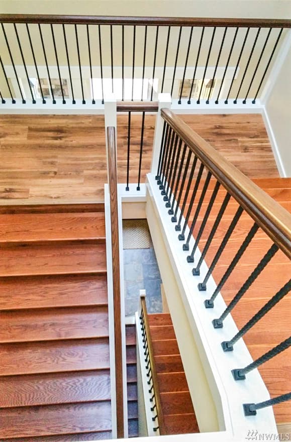 Interior view of a staircase with wood treads, white risers, and black metal balusters. Wood flooring visible on landings.