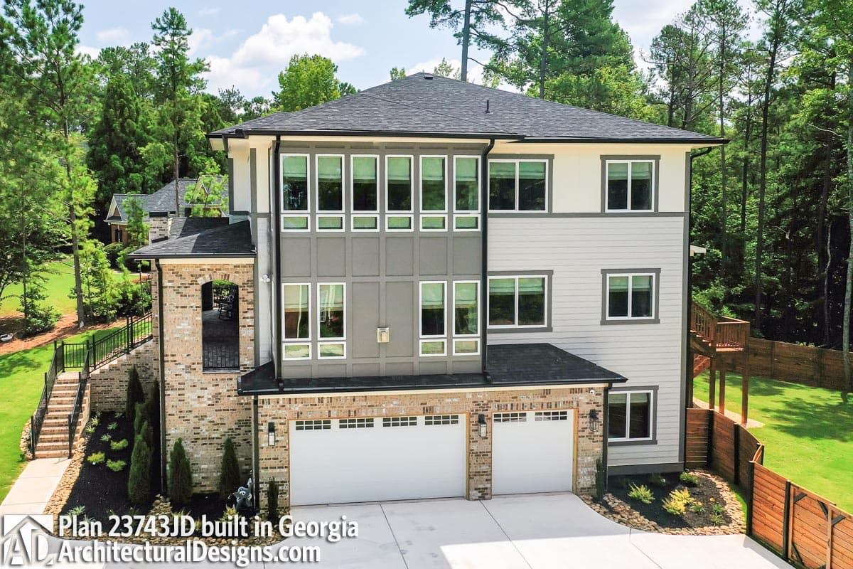 House plan exterior: Modern home with three stories, a brick-clad lower level, a two-car garage, and numerous large windows.