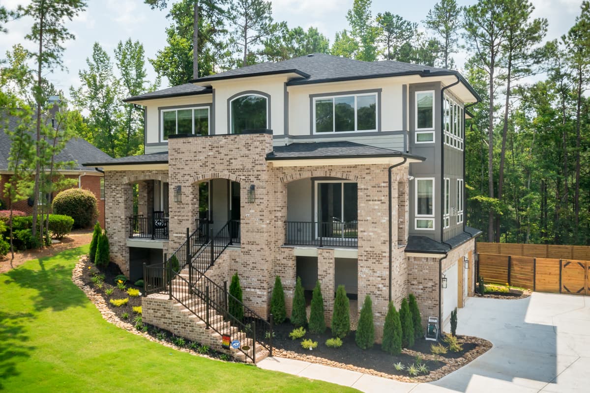 Two-story house plan exterior featuring a brick facade, arched porch, multi-pane windows, and a detached garage.