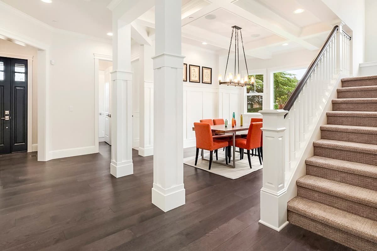 Interior view of a house foyer with a dining area, staircase, dark wood floors, and a black front door.