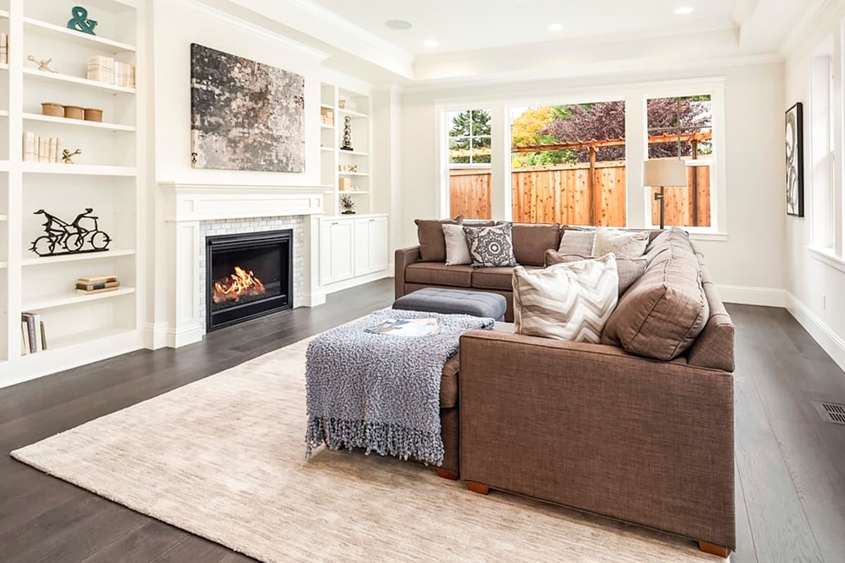 Living room with fireplace, built-in bookshelves, sectional sofa, and large windows overlooking a wooden fence.