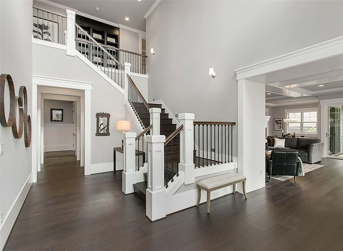 Interior view of a two-story foyer with a dark wood staircase, white balusters, dark railings, and an open view to a living room.