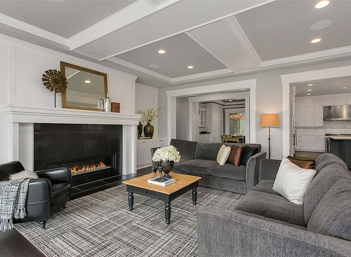 Living room interior with coffered ceiling, fireplace, sectional sofa, and view into kitchen and dining area.