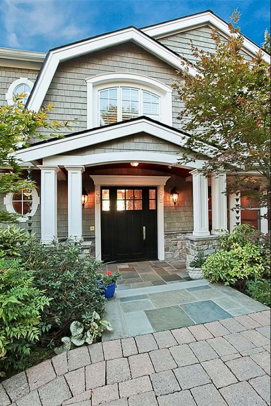 House plan exterior: Traditional style with shingle siding, arched window, gabled dormers, and covered porch with stone base.