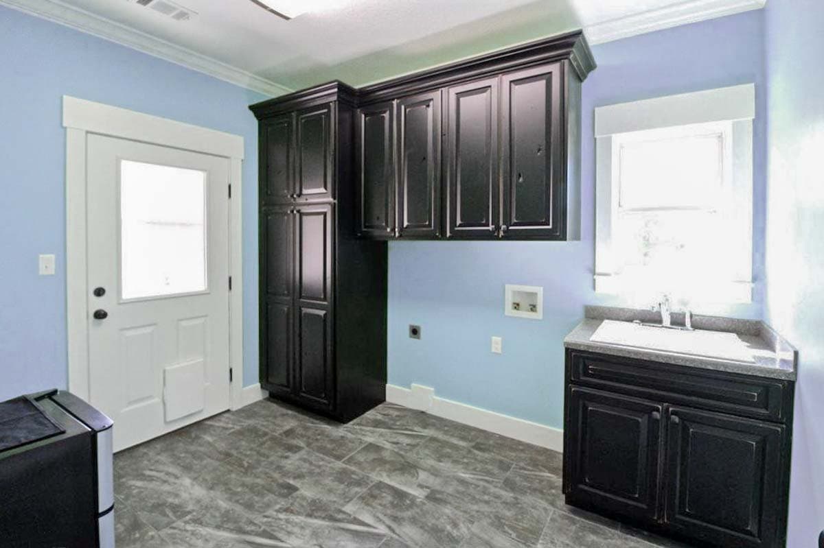 Laundry room with dark cabinetry, sink, window, and exterior door with pet door.