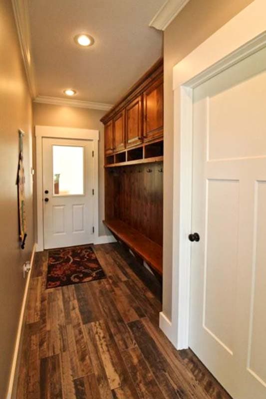 Mudroom with wooden bench, upper cabinets, coat hooks, glass-paneled door, and rustic wood-look flooring.