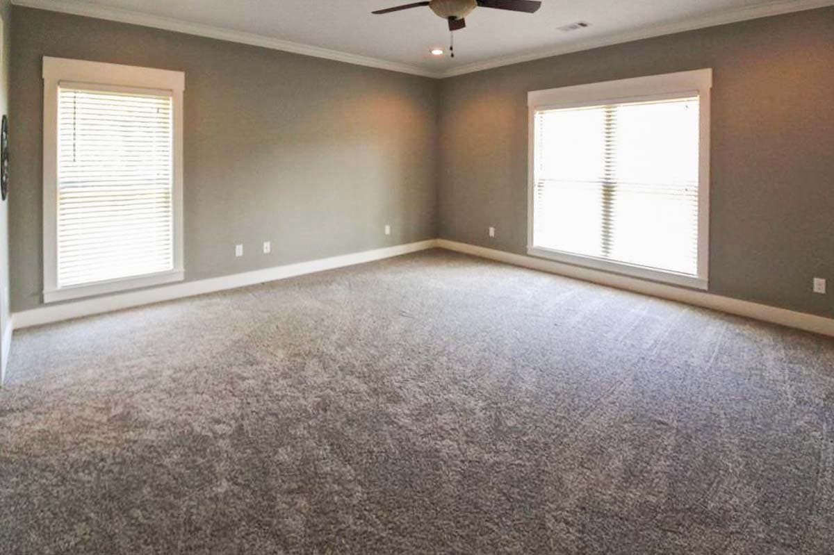 Interior view of a large, carpeted room with two windows, crown molding, and a ceiling fan.