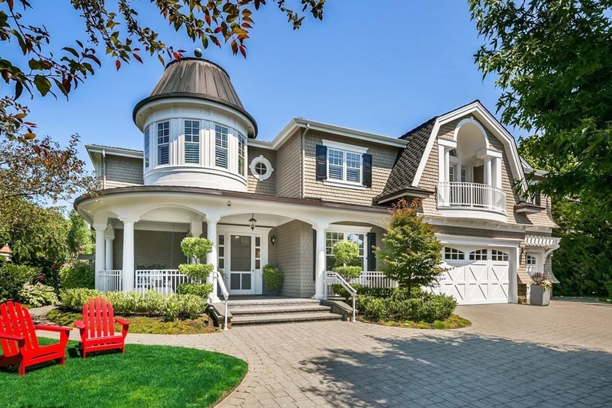House plan exterior featuring a two-story design with a turret, wraparound porch, and gabled rooflines with dormers. Garage visible on the right.