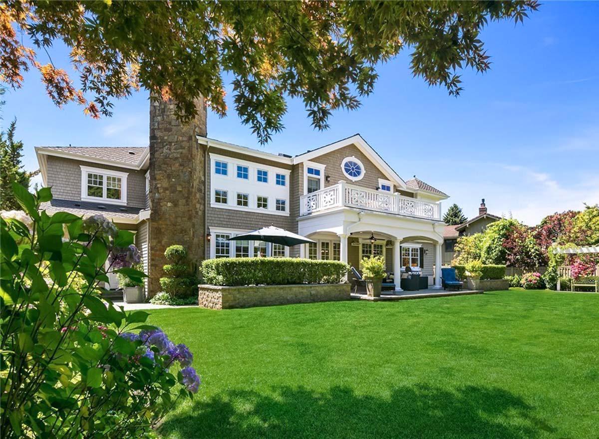 House plan exterior: two-story home with stone chimney, shingle siding, second-story balcony, and covered patio.
