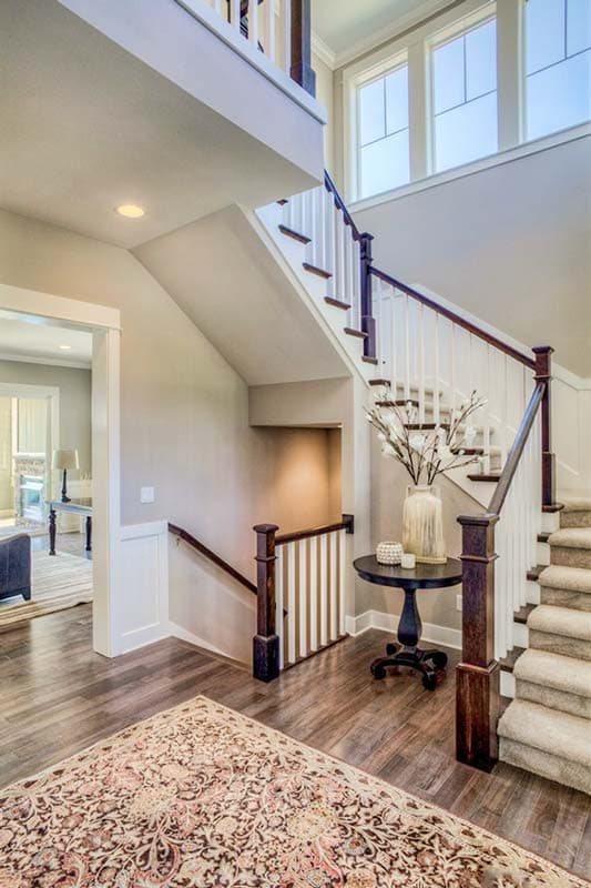 Interior view of a two-story foyer with a carpeted staircase, dark wood newel posts, white balusters, and a landing with a decorative table.