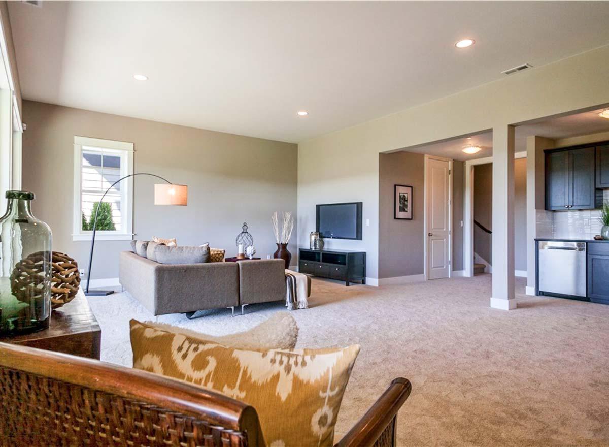 Interior view of a house plan showing a living area with a sectional sofa, television, and open access to a kitchen area with dark cabinets.