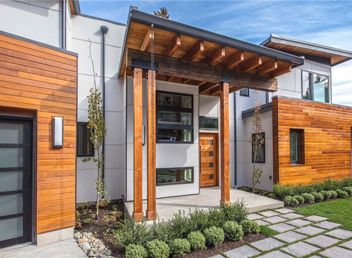 Modern house exterior with wood siding, covered entryway with exposed beams, and a glass garage door.