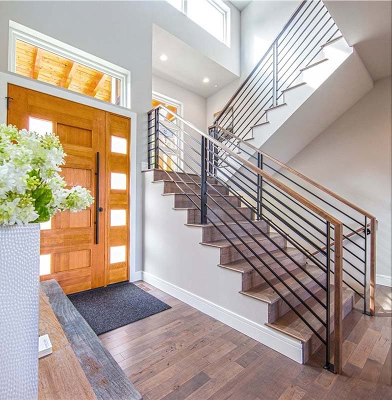 Interior view of a modern foyer with a double wooden door, floating staircase with black metal railing, and hardwood floors.