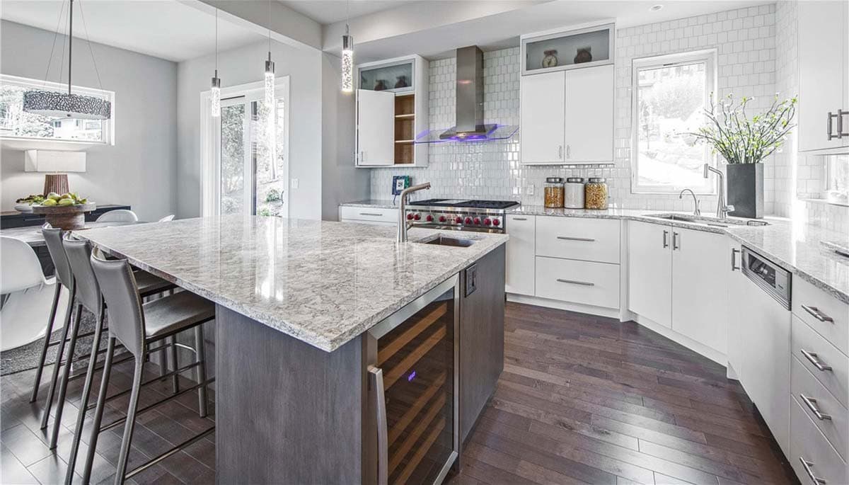 Contemporary kitchen with large island, wine fridge, stainless steel range hood, white shaker cabinets, and subway tile backsplash.