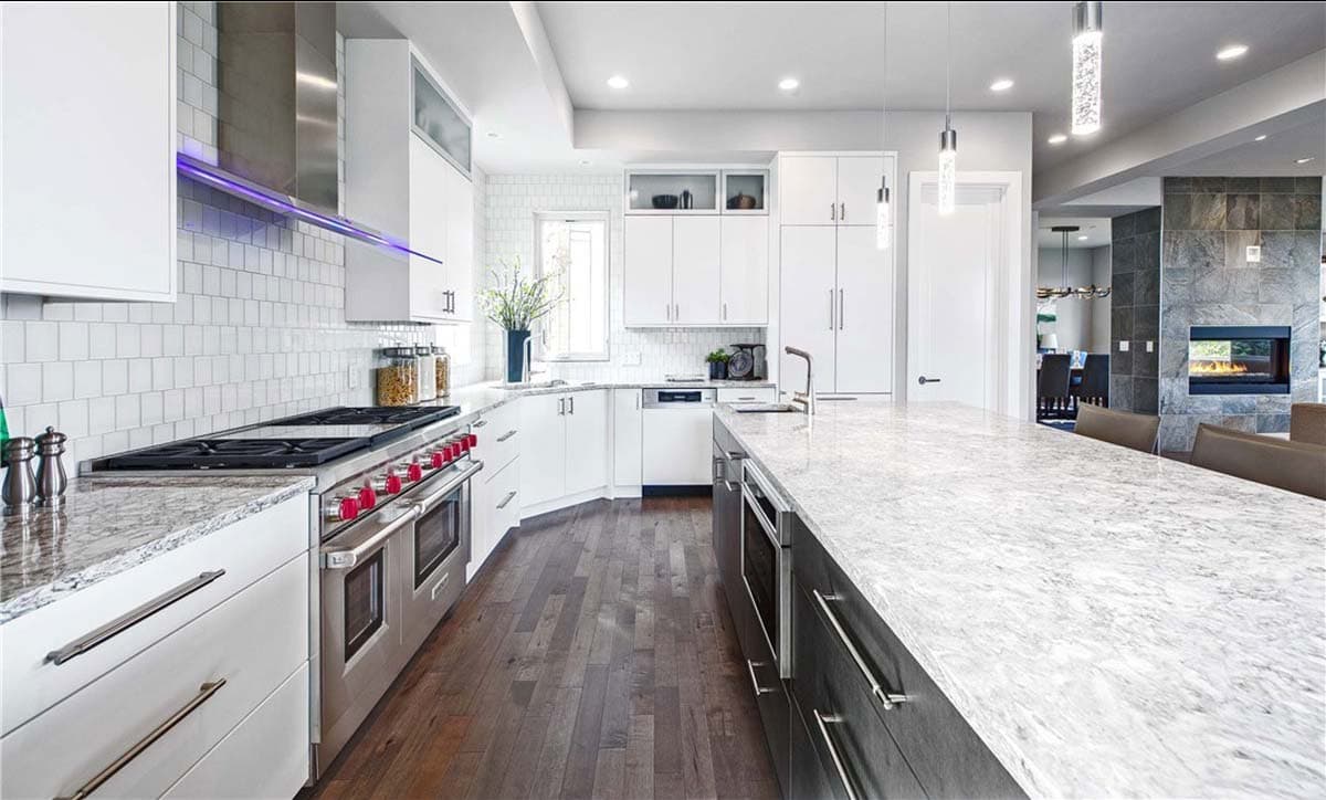 Modern kitchen with white cabinetry, stainless steel appliances, subway tile backsplash, large island, and a stone-clad fireplace.