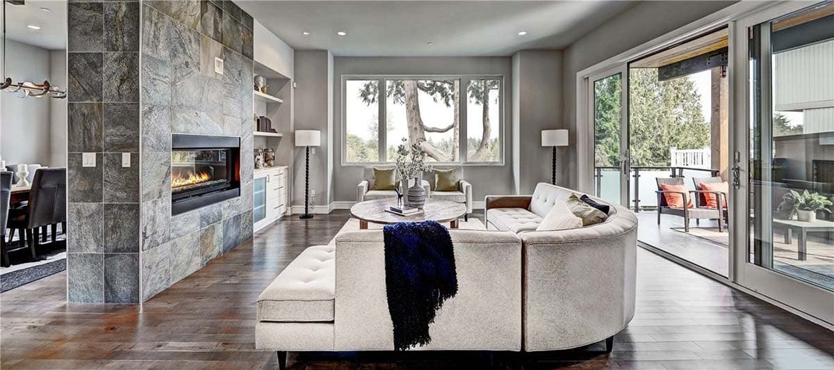 Interior view of a living room with a floor-to-ceiling stone fireplace, sectional sofa, and sliding glass doors.