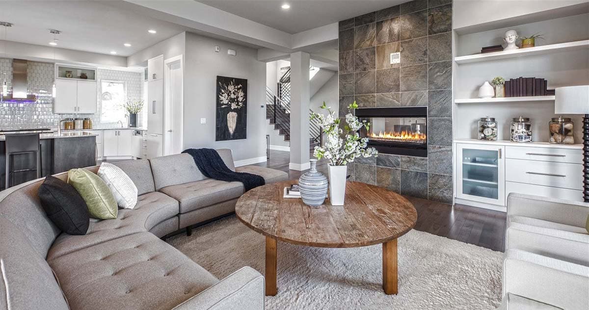 Living room with sectional sofa, fireplace, built-in shelving, and open access to kitchen and stairs.