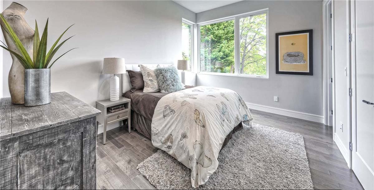 Bedroom with a queen bed, patterned comforter, corner windows, and wood flooring.