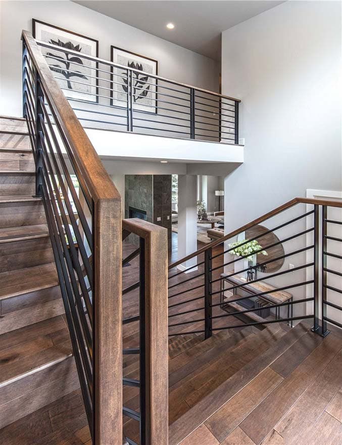 Interior view of open-concept home with wood staircase and black metal railings leading to second-floor landing with artwork.