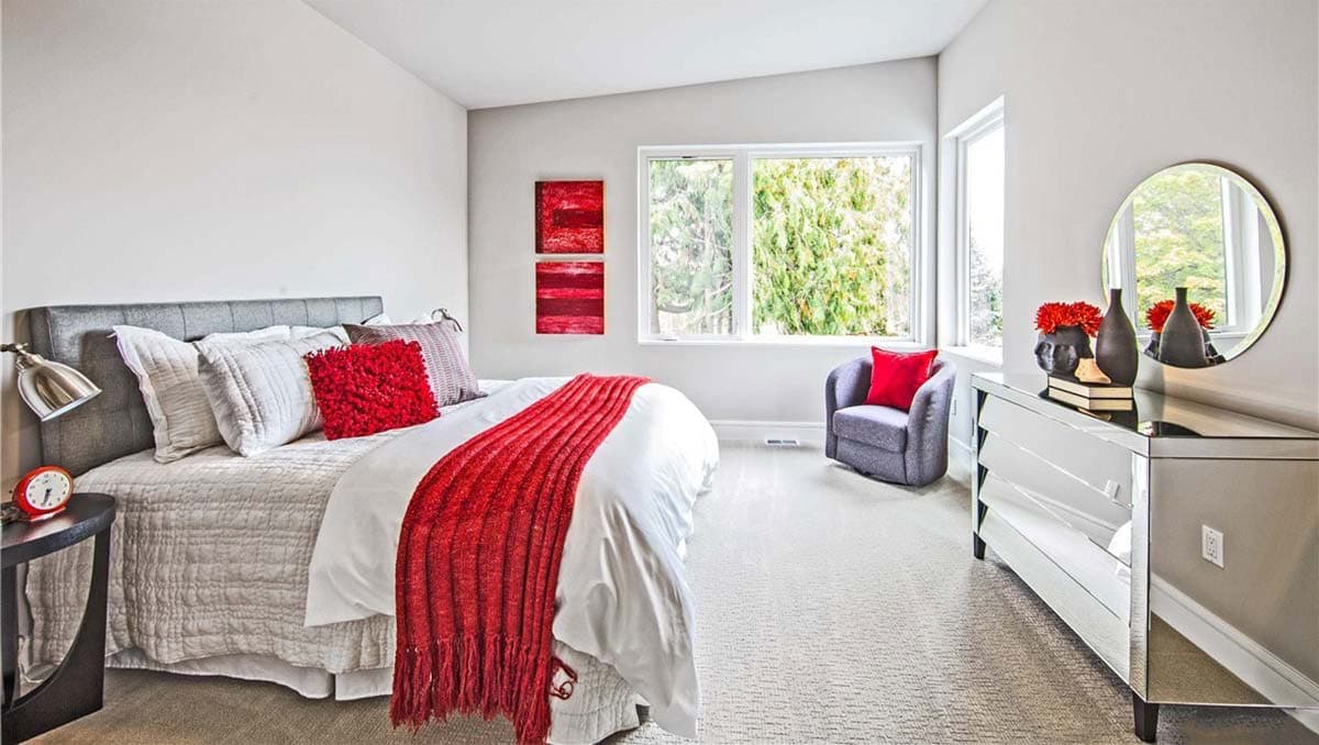 Bedroom interior with king bed, large window, gray armchair, and mirrored dresser.
