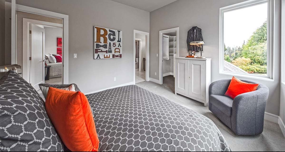 Bedroom with patterned bedding, a closet, and a window with a view. Open doorways reveal another room.