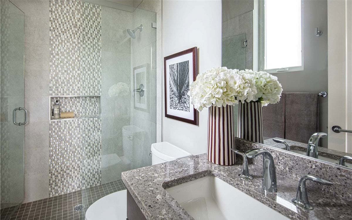 Bathroom with glass-enclosed shower featuring mosaic tile accent wall, granite vanity with dual sinks, and artwork.