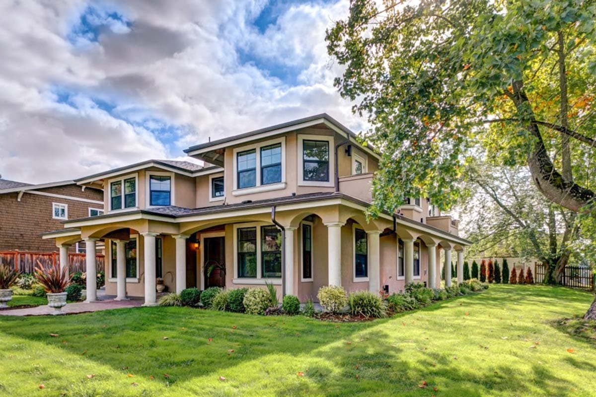 House plan exterior: Two-story home with a wraparound porch supported by Tuscan columns and multi-pane windows.