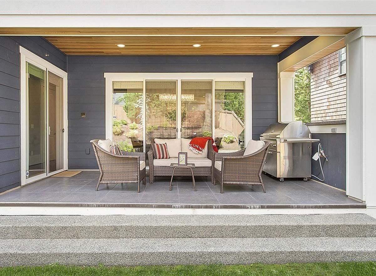 Covered patio with stone tile floor, outdoor seating, and stainless steel grill. Features wood-paneled ceiling.