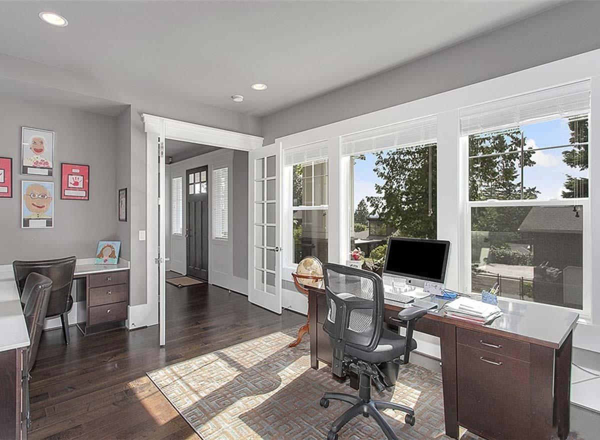 Home office with dual desks, large windows, and double doors leading to an entryway with a glass-paneled door.