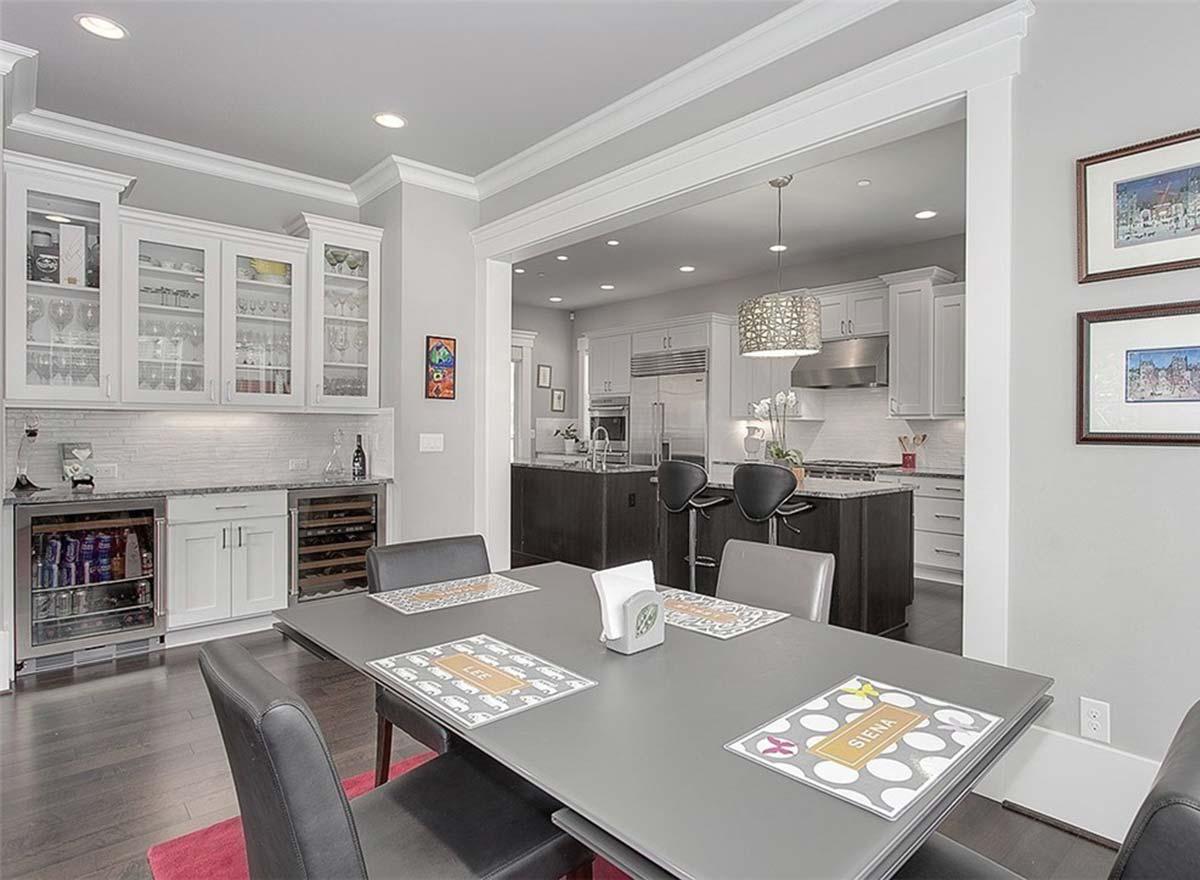 Dining area with table and chairs connected to modern kitchen with dark island, bar seating, and stainless steel appliances.