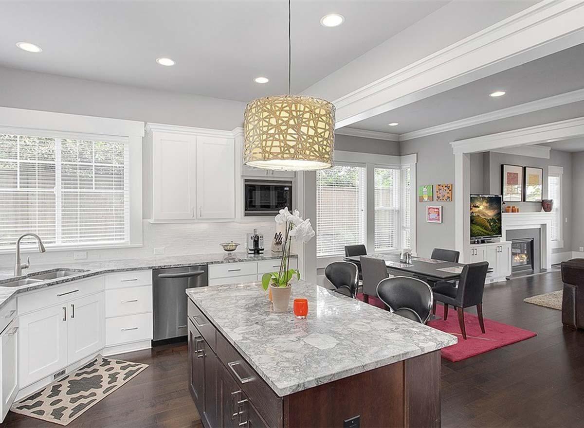 Modern kitchen with island, white cabinetry, granite countertops, stainless steel appliances, and adjacent dining area with fireplace.
