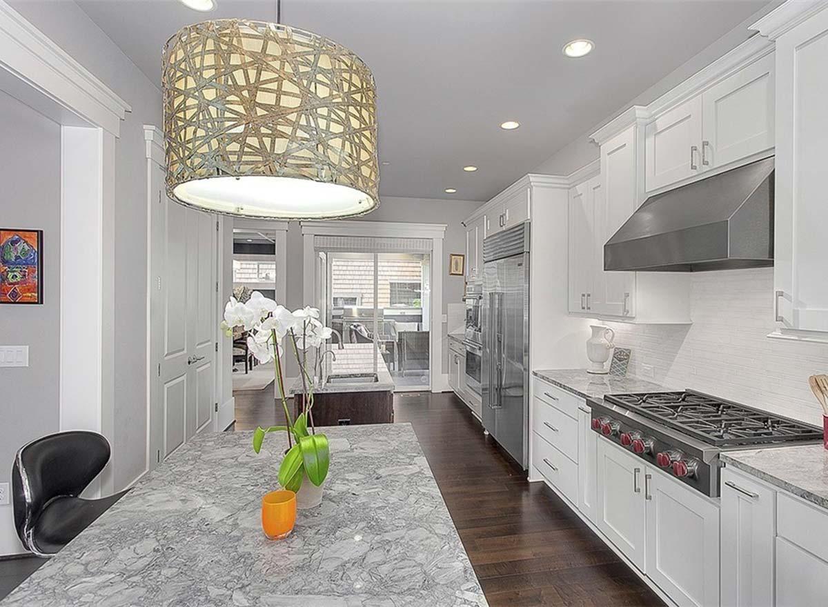 Contemporary kitchen with white cabinets, stainless steel appliances, marble island, and dark wood floors.