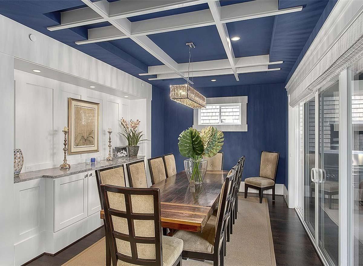 Dining room with dark wood table, upholstered chairs, built-in buffet, coffered blue ceiling, and sliding glass doors.