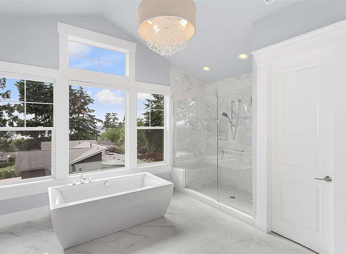 Bathroom interior with freestanding tub, glass-enclosed shower with marble tile, and large windows with vaulted ceiling.