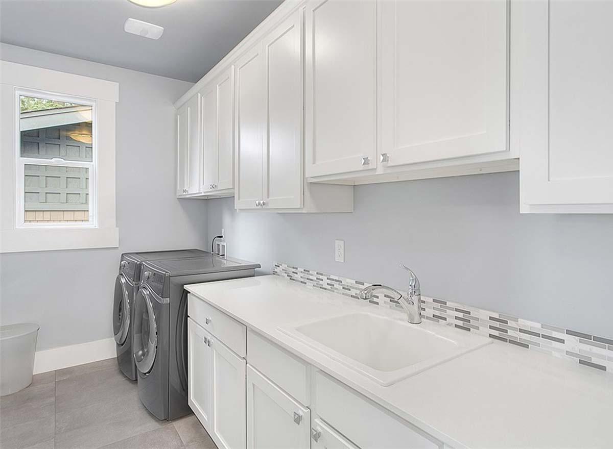 Laundry room with white cabinets, washer, dryer, sink, and a window with a view of the exterior.