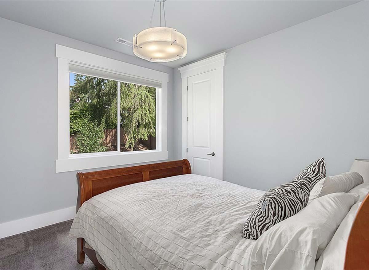 Interior bedroom with a wood-frame bed, white bedding, a large casement window, and a modern drum pendant light.