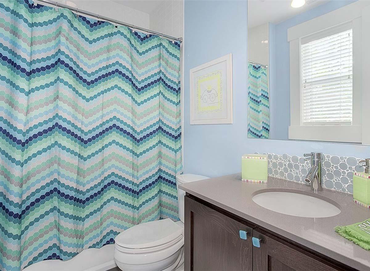 Bathroom with blue walls, chevron shower curtain, single vanity with gray countertop, and white-framed window.