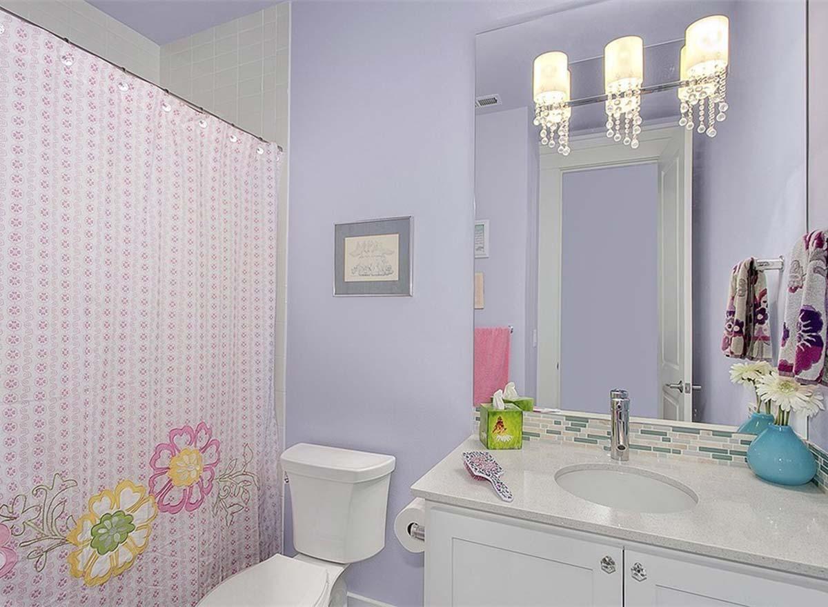 Bathroom with floral shower curtain, white toilet, vanity with stone countertop, and decorative light fixture.
