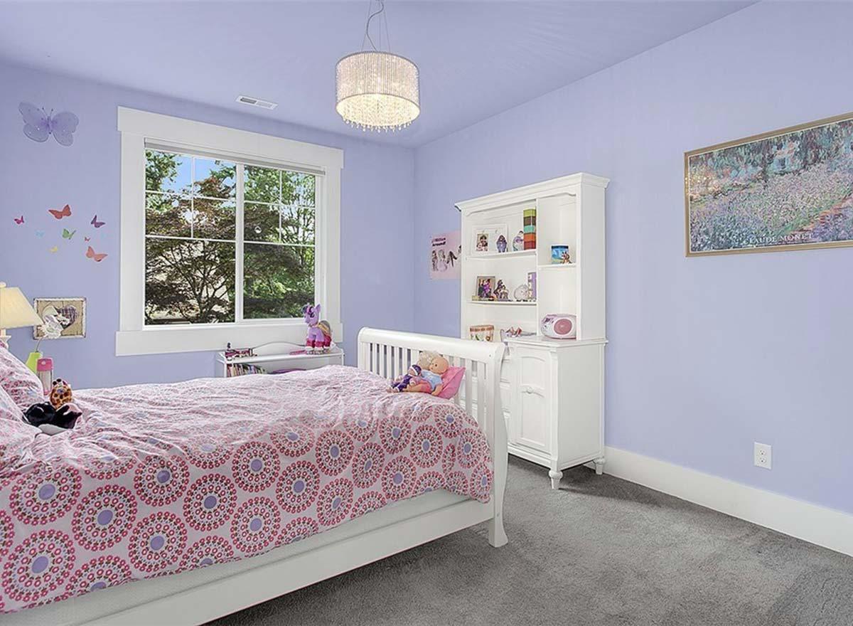 Bedroom interior with white crib, patterned bedding, large window with greenery view, and white hutch.