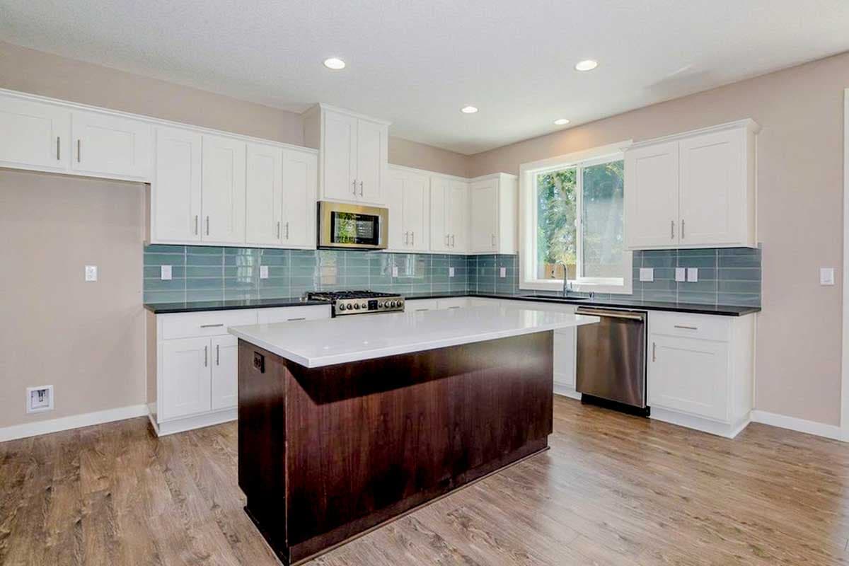 Kitchen interior with white cabinets, dark wood island, subway tile backsplash, stainless steel appliances, and large window.