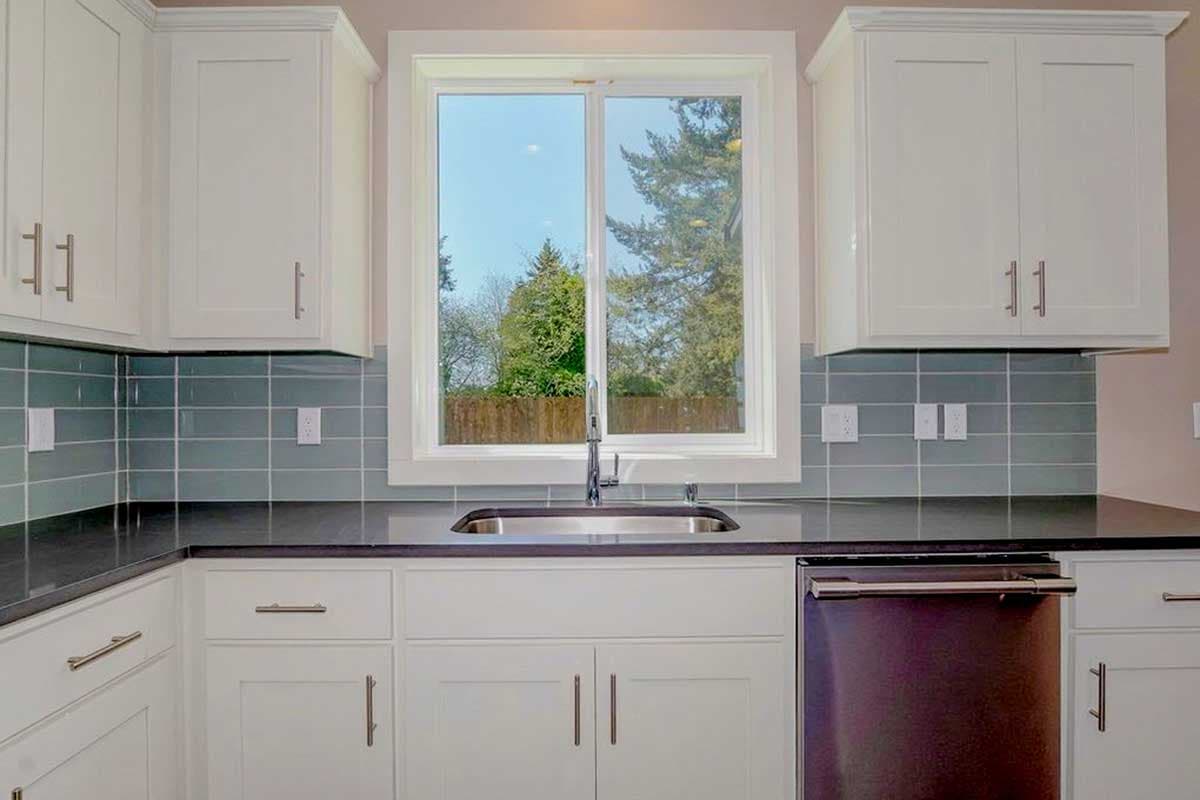 Kitchen with white cabinets, dark countertops, subway tile backsplash, and sink below a double-hung window.